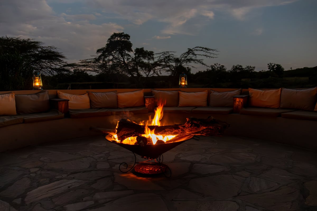 A cozy fire pit burns brightly, surrounded by comfortable seating in an outdoor lounge area at dusk
