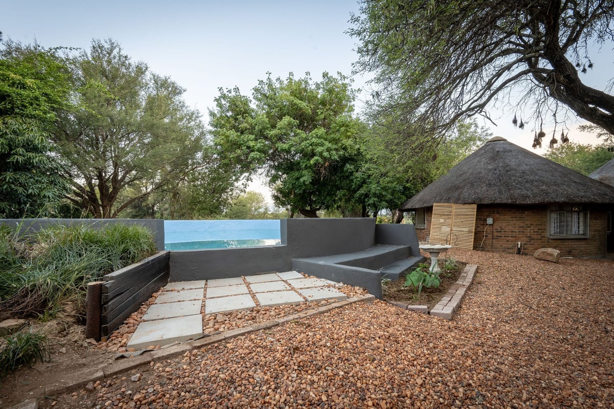 Modern concrete and gravel patio area with pool structure beside a brick building surrounded by trees