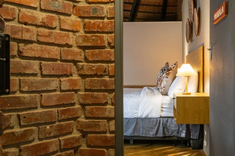 View through doorway of cozy bedroom with brick wall, bed with white linens, bedside table with lamp, and wooden flooring