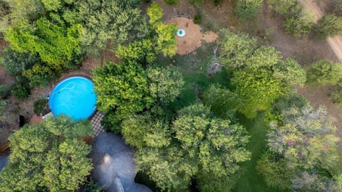 Aerial view of a bright blue circular pool surrounded by dense green forest and trees