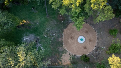 Aerial view of a circular clearing in a forest with a blue structure in the center, surrounded by dense green trees