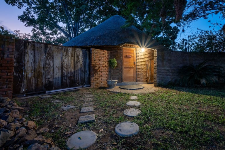 Small brick house at dusk with warm lighting, surrounded by trees, stone pathway, and grassy yard