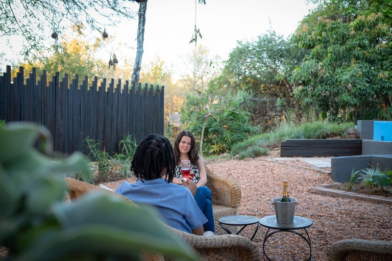 Two people sitting in a garden patio area with wooden fences, plants, and natural ground cover on a sunny day