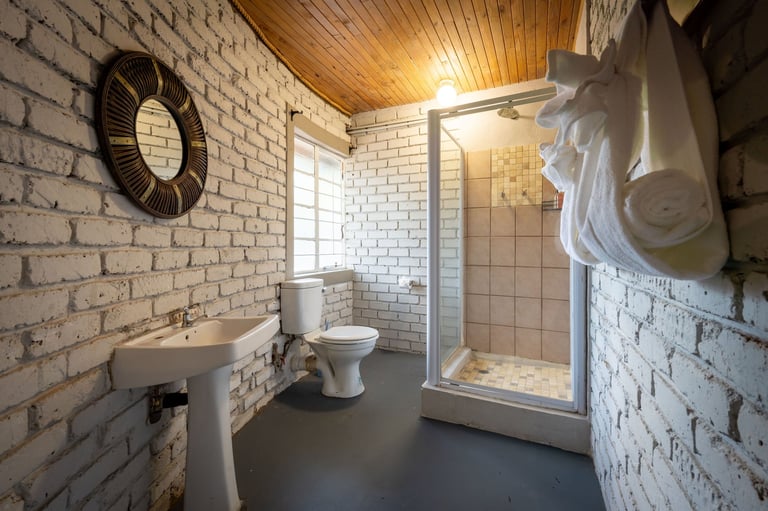 Modern bathroom with white subway tile walls, pedestal sink, toilet, glass shower enclosure, and wooden ceiling