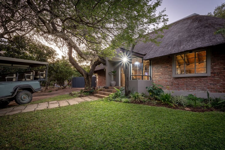 Modern brick home with thatched roof, manicured lawn, illuminated porch, and vintage truck parked on driveway at dusk