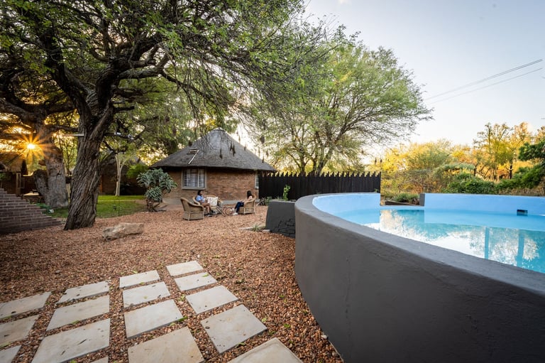 Backyard oasis with modern pool, stepping stone pathway, rustic cottage, and mature trees at dusk