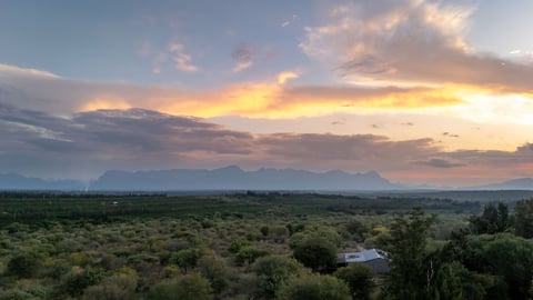 Dramatic sunset over vast savanna landscape with distant mountains and scattered trees under golden and purple clouds