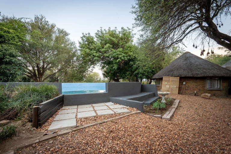 Modern infinity pool with blue water feature next to a brick building surrounded by trees and gravel landscaping