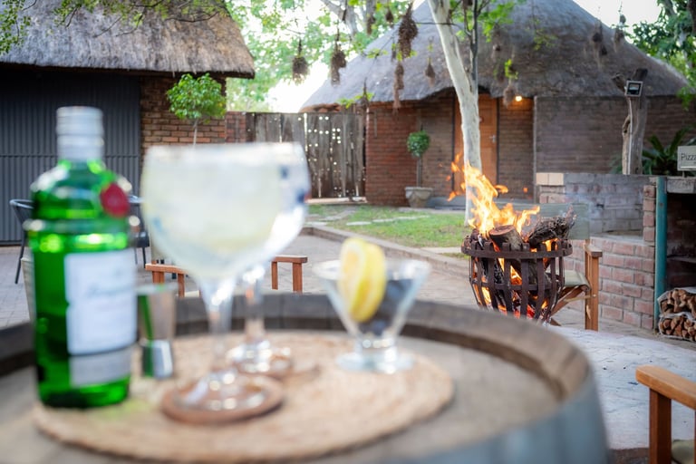 Cocktail with lemon slice in foreground with rustic courtyard, fire pit, and traditional thatched-roof buildings in background
