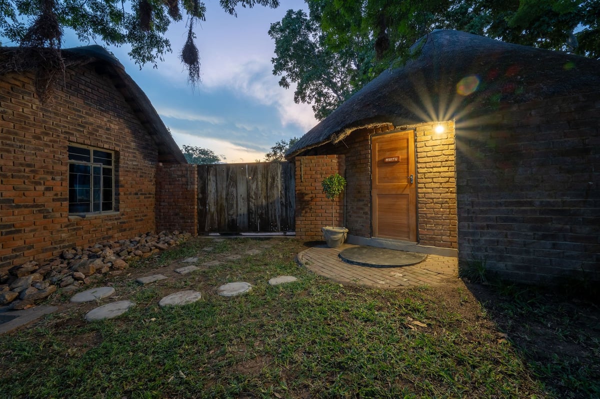 Backyard courtyard with brick buildings at dusk, showing stepping stones, green grass, and warm outdoor lighting