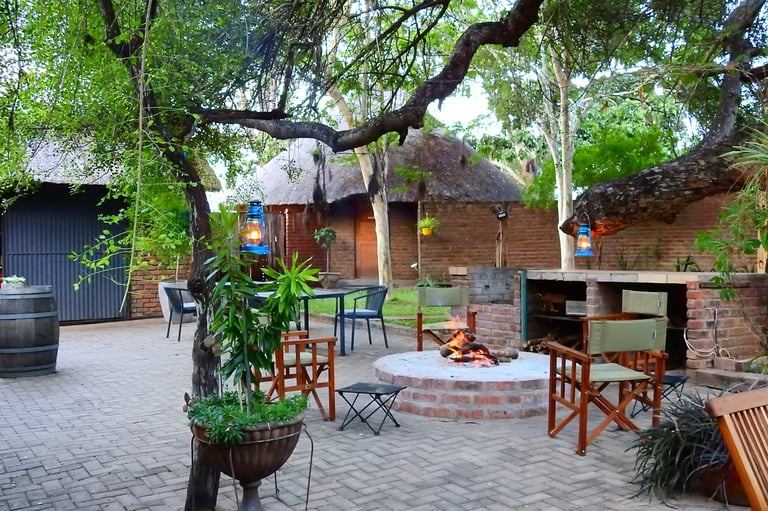 Outdoor brick patio with rustic fireplace, seating area under large tree, and hanging lights